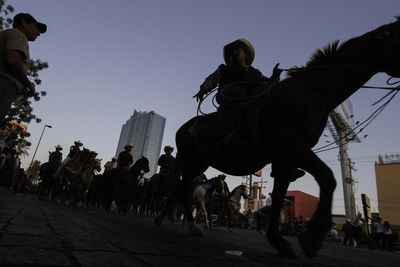 People riding horses in city against sky