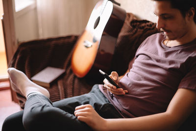 Serious young man using smart phone while sitting at home