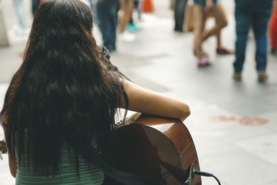 Rear view of woman playing guitar on street in city