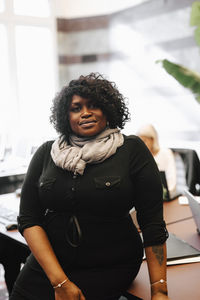 Portrait of businesswoman with curly hair leaning on desk at law office