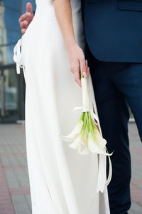 Midsection of couple holding hands while standing against white wall