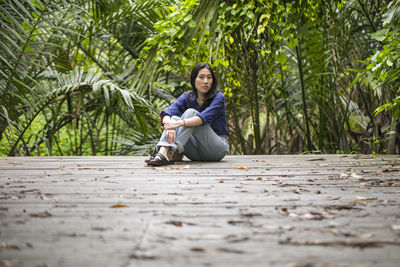 Portrait of young woman sitting on boardwalk against trees