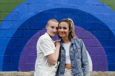 Lesbian couple standing together in front of colorful wall