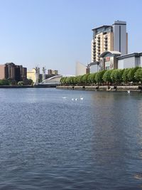 Buildings by river against clear sky