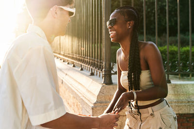 Cheerful black woman in stylish clothes laughing while dancing with boyfriend near road on sunlit city street