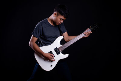 Full length of teenage girl playing guitar against black background