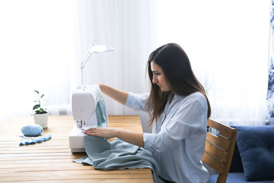 Charming girl with long black hair sews on a sewing machine, concept handmade and mother 