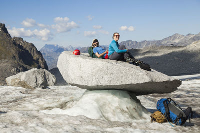 Couple sits on rock, snowbird glacier, talkeetna mountains, alaska