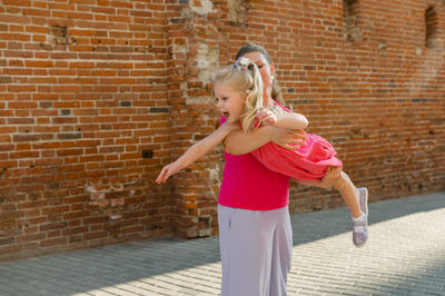 Side view of young woman standing against brick wall