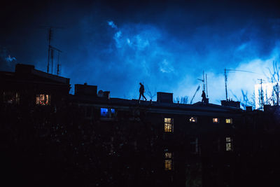 Low angle view of silhouette person walking buildings against cloudy sky at night