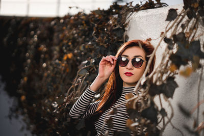 Portrait of young woman wearing sunglasses while standing by wall