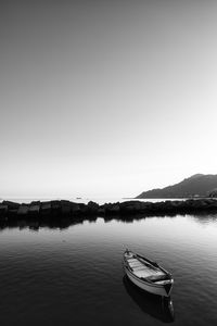 Boat moored in dock against clear sky in black and white