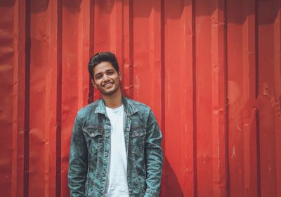 Portrait of smiling young man standing against red wall