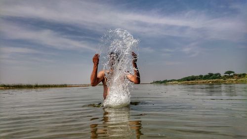 Low section of man splashing water against sky