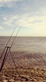 Fishing rods in sea against sky