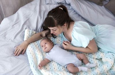 Young beautiful mother with her newborn baby boy lying in bed at home. top view. selective focus.