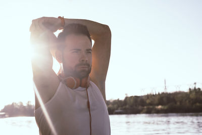 Young man with arms raised standing against lake