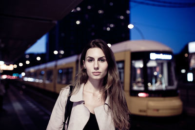 Portrait of young woman standing against train at railroad station