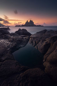 Rocks on beach against sky during sunrise