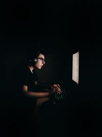 Side view of woman sitting against black background