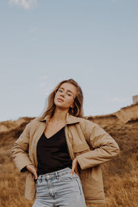 Portrait of young woman standing by plants against sky