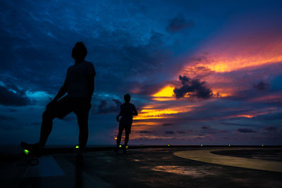 Silhouette friends on sea against sky during sunset