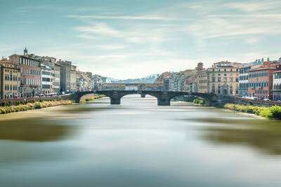 Arch bridge over river amidst buildings in city against sky