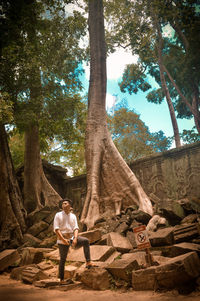 Full length of man sitting on tree trunk in forest