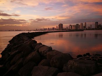 Scenic view of sea by buildings against sky during sunset