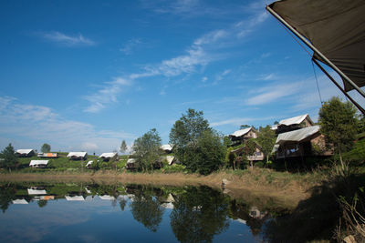 Reflection of trees and houses on lake against sky