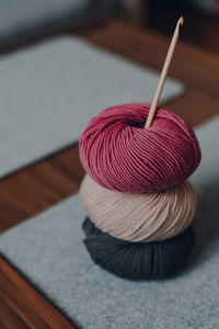 Three different coloured balls of dk yarn with a wooden crochet hook on a table, shallow focus.