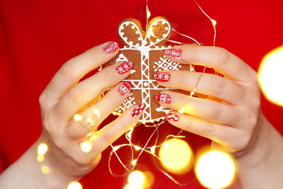 Midsection of woman holding illuminated string light with christmas cookie