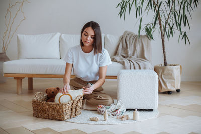 A tired young woman sits on a white carpet in the living room 