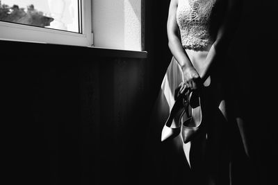 Midsection of bride holding shoes while standing in darkroom
