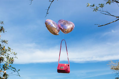 Low angle view of red paragliding hanging against sky