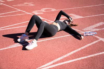 High angle view of tired woman lying with water bottle on running track