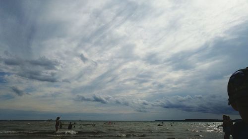 Rear view of man standing on beach against cloudy sky