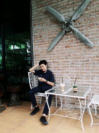 Man using phone while sitting at outdoor cafe against brick wall