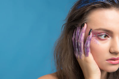 Close-up of young woman wearing make-up while looking away against blue background