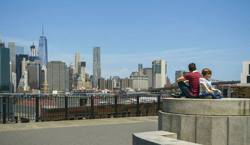 Men sitting on railing against buildings in city