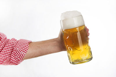Cropped hand of person holding beer glass against white background