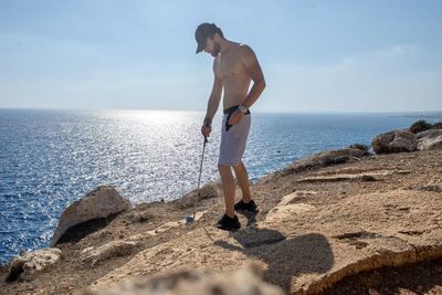 Full length of man standing on rock at beach against sky