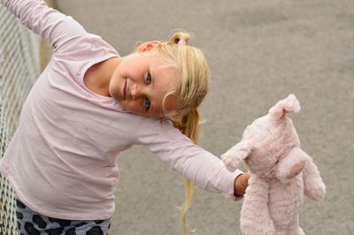 Portrait of girl holding teddy bear while standing on footpath