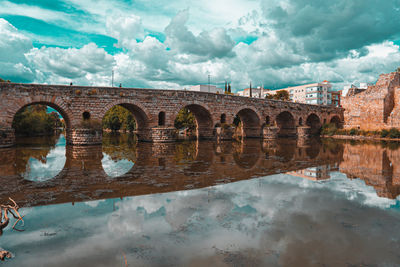 Arch bridge over river against cloudy sky