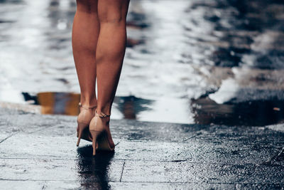 Low section of woman wearing high heals standing on footpath by lake