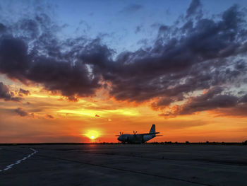 Airplane on runway against sky during sunset