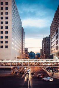 Vehicles on road by buildings against sky during sunset