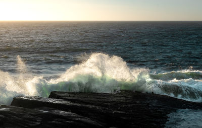 Waves splashing on rocks against clear sky