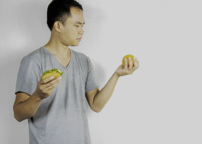 Man looking at orange while holding burger while standing against white background