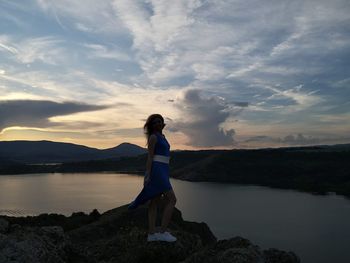 Woman standing on rock against sky during sunset